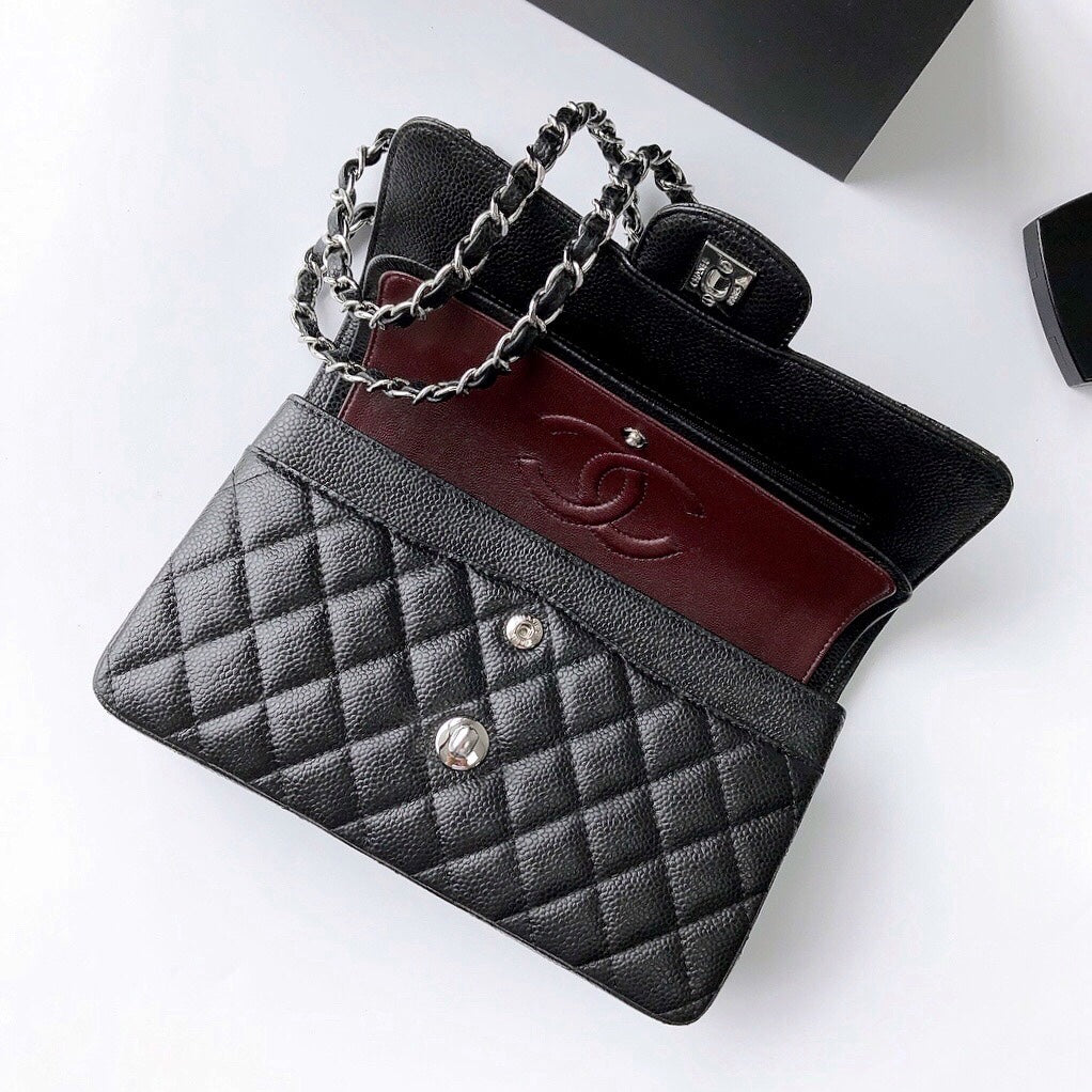 A luxury quilted black leather handbag with a dark red leather interior lining, silver-tone chain strap, and silver hardware, displayed on a clean white surface.