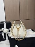 A Chanel mini bucket bag in off-white quilted leather with gold-tone chain straps and a gold interlocking CC logo, displayed on a black box next to its branded black presentation box with a white ribbon.